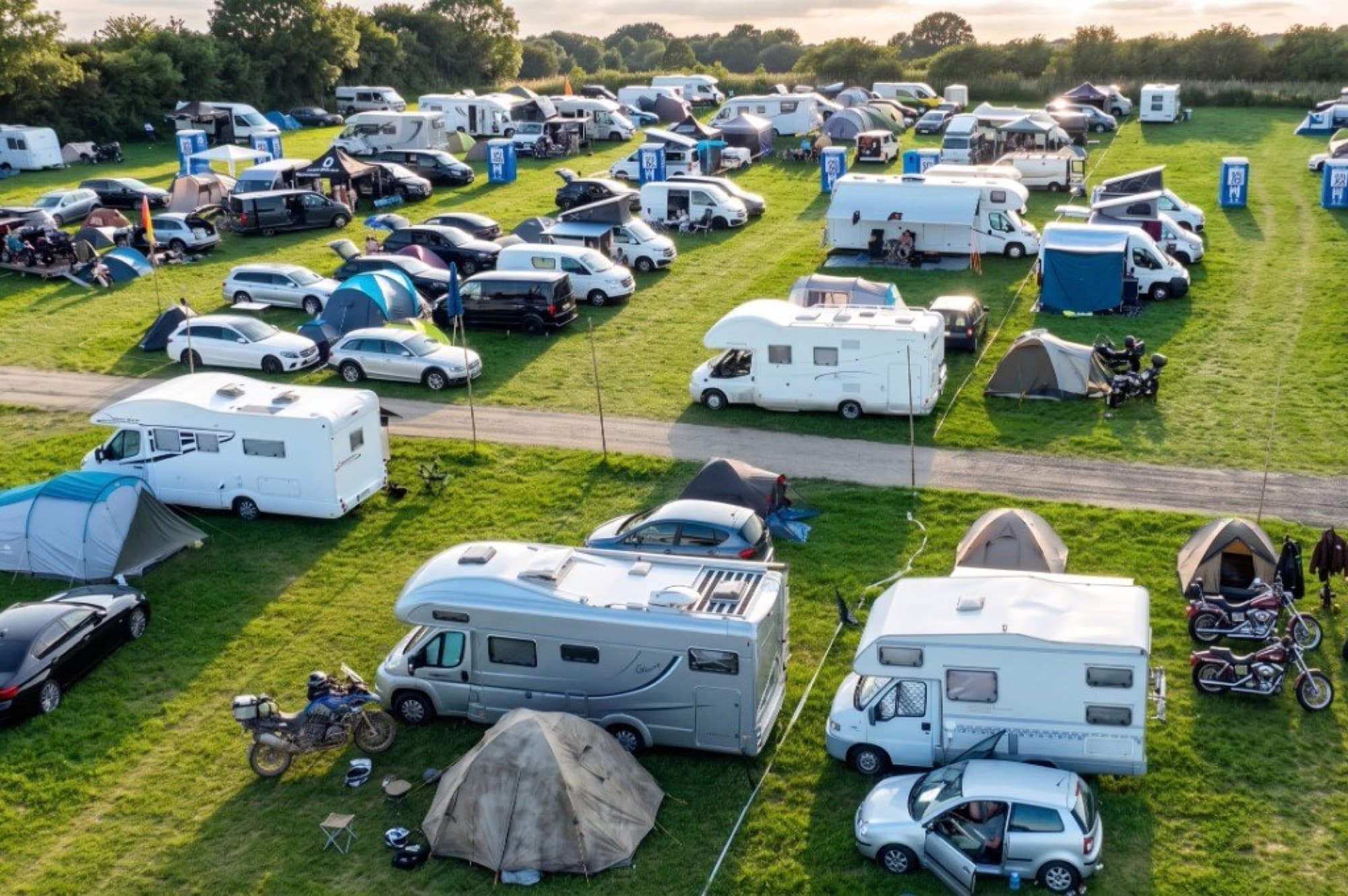Luftbild der Eventcamping-Stellplätze bei Abendlicht: Wohnmobile, Zelte und Motorräder in dichten Reihen